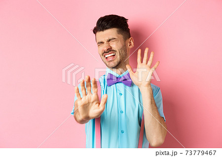 Crying guy asking to stop, raising hands up in defense, protecting himself from assault, standing over pink background 73779467