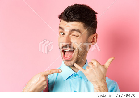 Cheeky and funny guy showing phone gesture, asking to call him and winking, telling dial his number, standing over pink background 73779470
