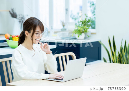キッチンでノートパソコンを使うメガネの女性 73783390