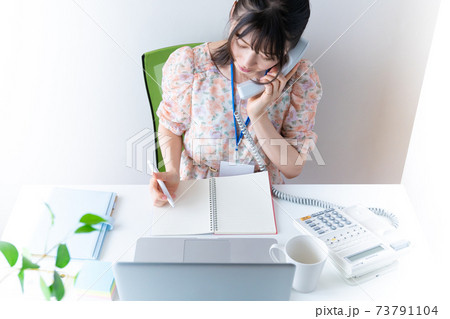 電話をかけながらPCで仕事をするワンピースを着た若い女性 電話をかけながらPCで仕事をするワンピースを着た若い女性 73791104