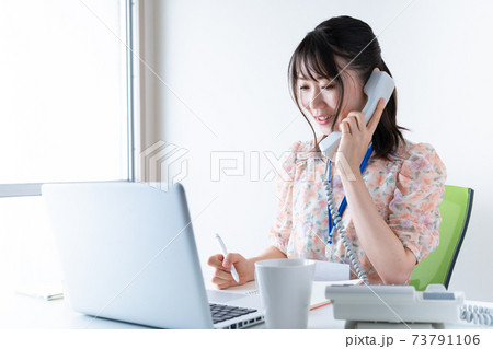 電話をかけながらPCで仕事をするワンピースを着た若い女性 電話をかけながらPCで仕事をするワンピースを着た若い女性 73791106