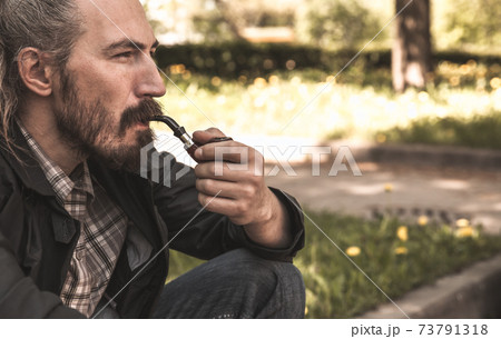 Brutal bearded man smokes a pipe in summer park 73791318