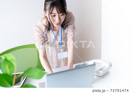 デスクの前で立ちながらPCを操作するワンピースを着た若い女性 デスクの前で立ちながらPCを操作するワンピースを着た若い女性 73791474