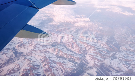Air plane flies among the clouds over snowy capped mountains. 73791932