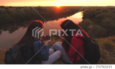 Female travelers sit high on a mountain by the river at sunset and drink tea from a mug. Go camping with a friend on the weekend. Tourist exploration of the area of nature. Free yourself from everyday 73792035