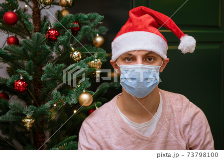 young man near a Christmas tree at home wearing a mask and hat of Santa Claus young man near a Christmas tree at home wearing a mask and hat of Santa Claus 73798100