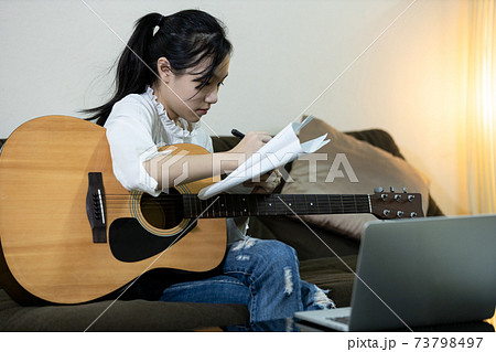 Asian child girl who is serious about composing a song hands writing song on textbook,female people hold a guitar,student study and learn from the internet,online guitar teaching courses with computer 73798497