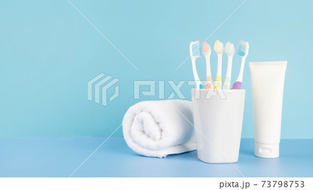Toothbrushes in a glass with toothpaste and towel on light blue table in bathroom. Dental health care and oral hygiene concept. Copy space. Toothbrushes in a glass with toothpaste and towel on light blue table in bathroom. Dental health care and oral hygiene concept. Copy space. 73798753