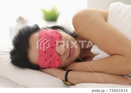 Woman lies on bed with mask over her eyes Woman lies on bed with mask over her eyes 73801614