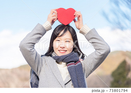 青空の下で頭の上にハートの箱を掲げる女性の写真素材