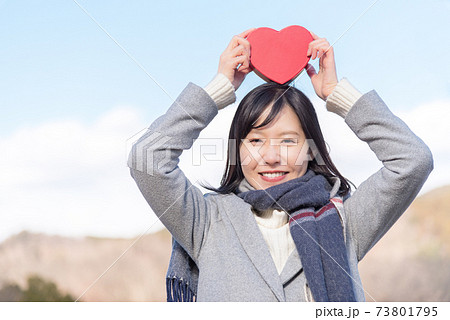 青空の下で頭の上にハートの箱を掲げる女性の写真素材