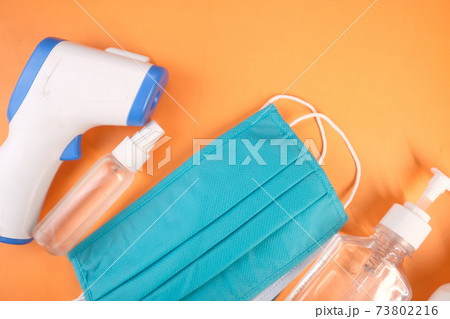 Surgical masks, thermometer and hand sanitizer on orange background Surgical masks, thermometer and hand sanitizer on orange background 73802216