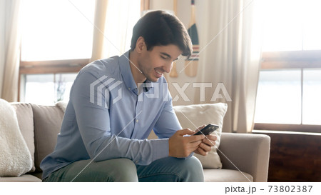 Close up smiling man using phone, sitting on cozy couch 73802387