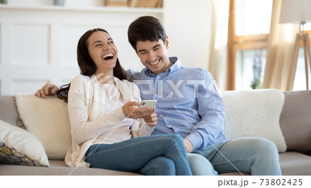 Happy young couple using phone, laughing, having fun together Happy young couple using phone, laughing, having fun together 73802425