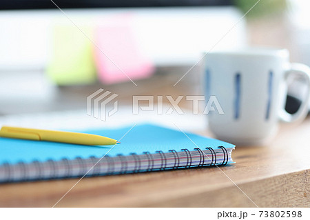 On table is cup next to pen and diary for notes 73802598