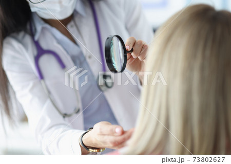 Dermatologist examines patient's face through magnifying glass Dermatologist examines patient's face through magnifying glass 73802627