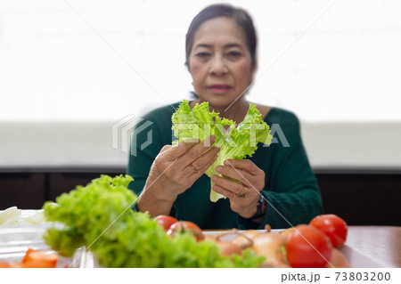 Senior woman prepare green salad from lettuce and tomato. 73803200