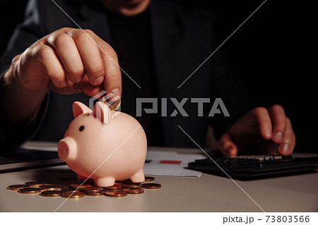 Businessman is counting profit on a calculator in office, piggy bank with coins at desk 73803566