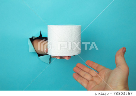 Female hand out of hole in the paperman, holding a roll of toilet paper. Isolate on blue background 73803567