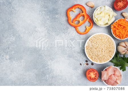 Raw ingredients for cooking pilaf, Brown rice and chicken fillet, grated carrots and chopped onions, pepper tomato garlic herbs and spices. Gray background, top view. copy space Raw ingredients for cooking pilaf, Brown rice and chicken fillet, grated carrots and chopped onions, pepper tomato garlic herbs and spices. Gray background, top view. copy space 73807086