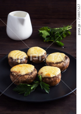 Baked mushrooms stuffed with cheese and herbs on a black plate. wooden background. 73807127