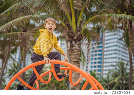 The boy climbs on the playground against the background of palm trees The boy climbs on the playground against the background of palm trees 73807653