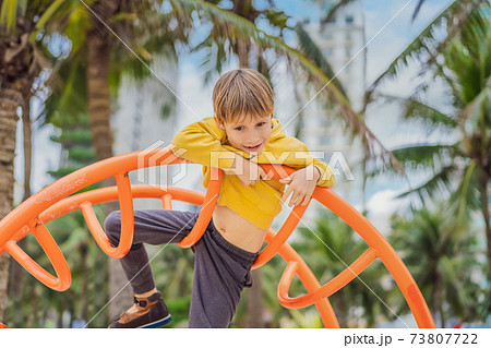 The boy climbs on the playground against the background of palm trees 73807722