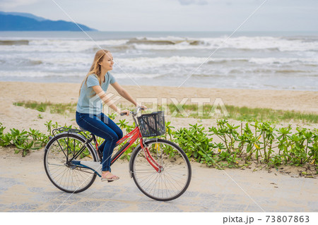 Young woman with bicycle enjoying a bike ride by the sea Young woman with bicycle enjoying a bike ride by the sea 73807863