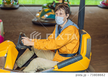 Man wearing a medical mask during COVID-19 coronavirus having a ride in the bumper car at the amusement park Man wearing a medical mask during COVID-19 coronavirus having a ride in the bumper car at the amusement park 73808662