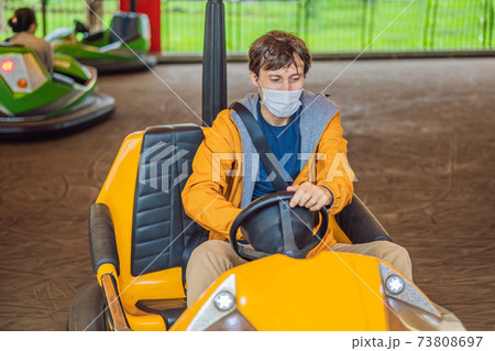 Man wearing a medical mask during COVID-19 coronavirus having a ride in the bumper car at the amusement park Man wearing a medical mask during COVID-19 coronavirus having a ride in the bumper car at the amusement park 73808697