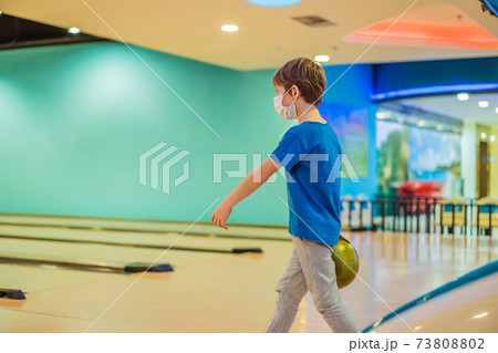 Boy playing bowling with medical masks during COVID-19 coronavirus in bowling club Boy playing bowling with medical masks during COVID-19 coronavirus in bowling club 73808802
