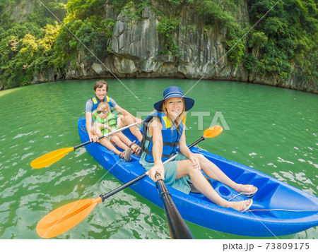 Mom, dad and son travelers rowing on a kayak in Halong Bay. Vietnam. Travel to Asia, happiness emotion, summer holiday concept. Traveling with children concept. After COVID 19. Picturesque sea Mom, dad and son travelers rowing on a kayak in Halong Bay. Vietnam. Travel to Asia, happiness emotion, summer holiday concept. Traveling with children concept. After COVID 19. Picturesque sea 73809175