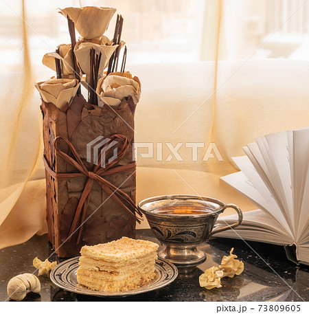 Homemade flowers from natural materials, Napoleon cake and a cup of tea on the windowsill. 73809605