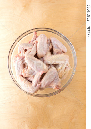Chicken wings in a glass bowl. A glass dish with raw wings on a wooden table. 73811062