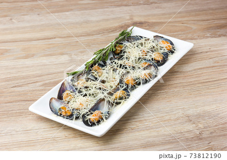 Fried mussels in the sink on a plate. Mussels in a sauce and grated Parmesan in a plate on a wooden table. 73812190