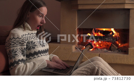 Young woman celebrates success or a happy pose with a laptop in front of a fireplace 73812730