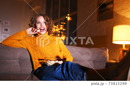 Positive woman with popcorn resting on sofa and watching TV 73815299