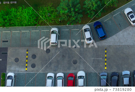 Above view of cars parked at car parking area of the apartment. Aerial view concrete car parking lot with speed bump near green trees in the park. Outdoor car parking space with empty slots. 73819280