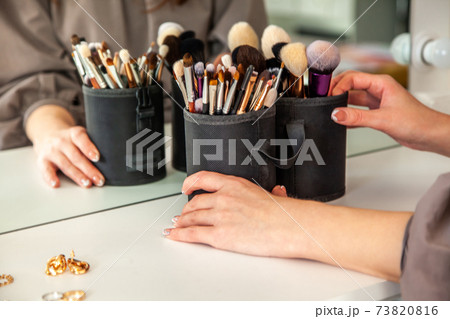 Woman hands is taking out makeup brush set from the drawer of vanity table. 73820816