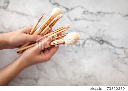 Female hands holding makeup brushes for powder or eyeshadow on coral colored background. Female hands holding makeup brushes for powder or eyeshadow on coral colored background. 73820820