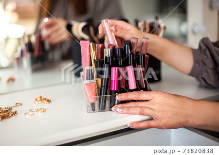 Young woman is neatly organizing her lipstick, lip gloss in the makeup storage at home. Young woman is neatly organizing her lipstick, lip gloss in the makeup storage at home. 73820838