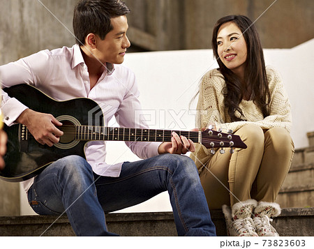 young asian lovers sitting on steps playing guitar and singing 73823603