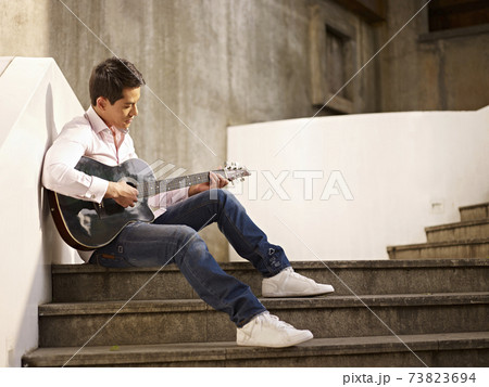 young asian man sitting on steps playing guitar and singing young asian man sitting on steps playing guitar and singing 73823694