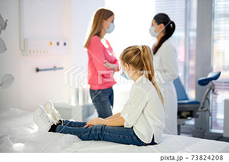 pretty caucasian sick child girl sits looking at mother talking with doctor in hospital 73824208