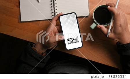 Top view of male hand holding smartphone and coffee cup on worktable Top view of male hand holding smartphone and coffee cup on worktable 73826534
