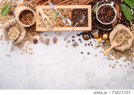 Green and brown decaf unroasted and dark roasted coffee beans in wooden box with scoops setup on white concrete background. Green and brown decaf unroasted and dark roasted coffee beans in wooden box with scoops setup on white concrete background. 73827335
