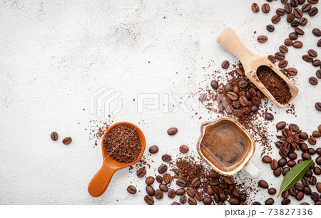 Background of various coffee , dark roasted coffee beans , ground and capsules with scoops setup on white concrete background with copy space. Background of various coffee , dark roasted coffee beans , ground and capsules with scoops setup on white concrete background with copy space. 73827336