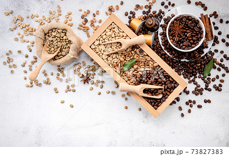 Green and brown decaf unroasted and dark roasted coffee beans in wooden box with scoops setup on white concrete background. Green and brown decaf unroasted and dark roasted coffee beans in wooden box with scoops setup on white concrete background. 73827383