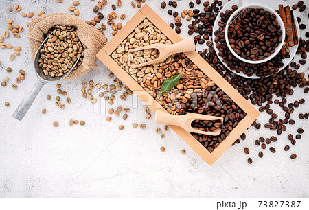 Green and brown decaf unroasted and dark roasted coffee beans in wooden box with scoops setup on white concrete background. Green and brown decaf unroasted and dark roasted coffee beans in wooden box with scoops setup on white concrete background. 73827387