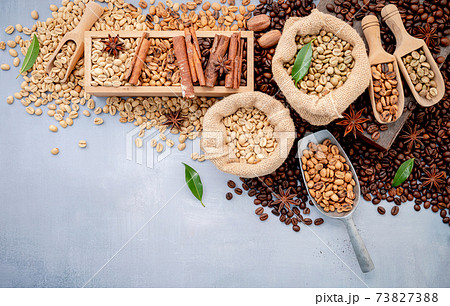 Green and brown decaf unroasted and dark roasted coffee beans in hemp sack bags with scoops setup on white concrete background. Green and brown decaf unroasted and dark roasted coffee beans in hemp sack bags with scoops setup on white concrete background. 73827388